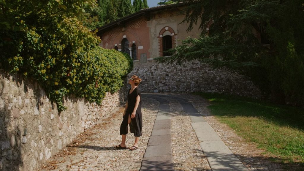 A woman walks along a stone path by a historic building in Lonato del Garda, Italy.